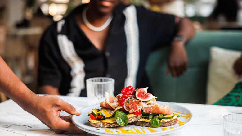 hand placing a plate of colorful bruschetta on a marble table in a cafe