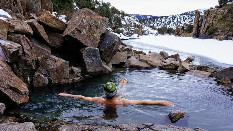 Man relaxing in riverside hot spring surrounded by snow