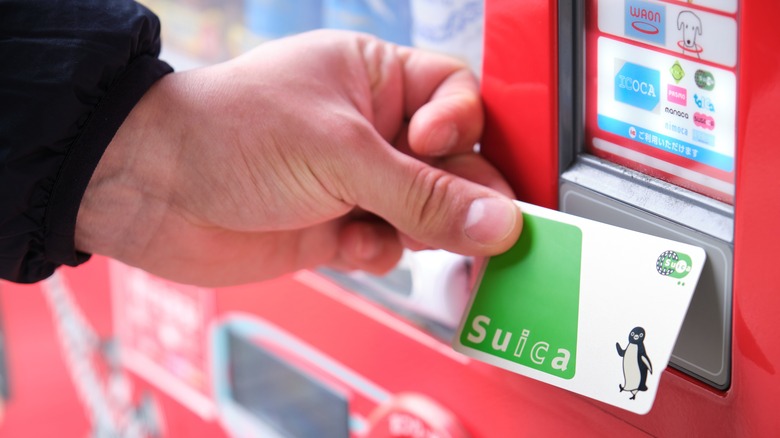 Man holds Suica card against vending machine.