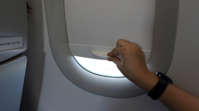 person closing window on plane