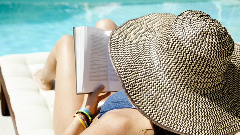 woman in sunhat reading near pool