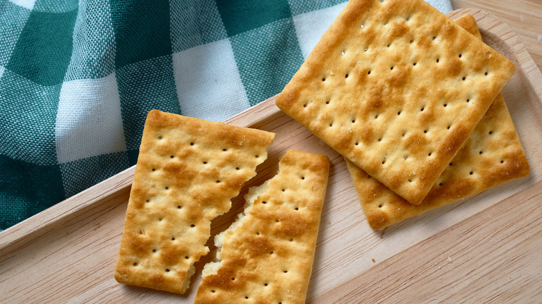 Two crackers, one broken in half, on wooden tray