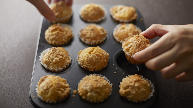 Two hands taking mini muffins from pan