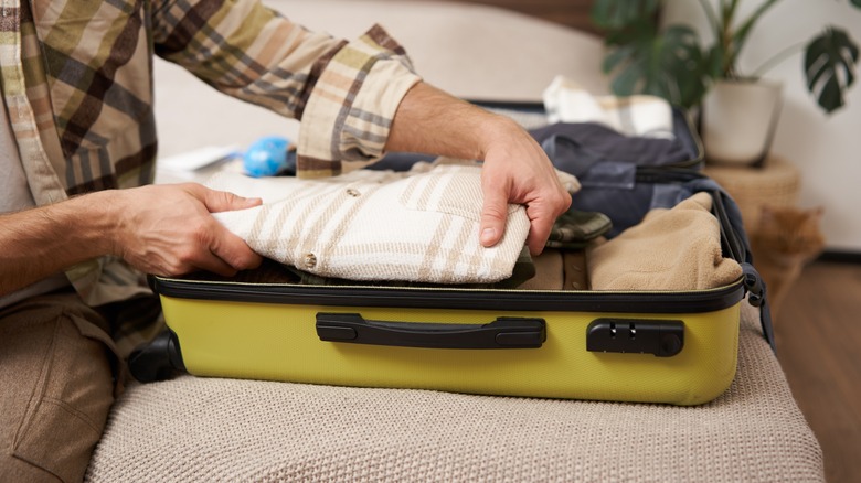 Man putting shirt in packed suitcase