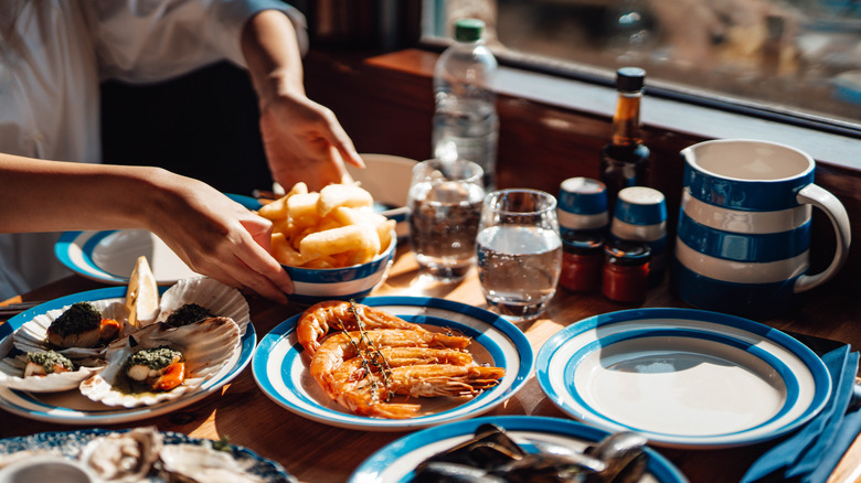 A person placing a bowl on a table full of seafood dishes