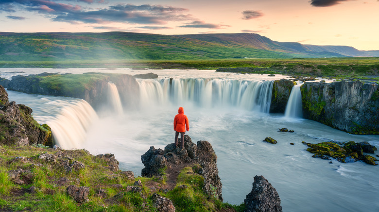 hiker in orange coat looks out over large waterfall Iceland