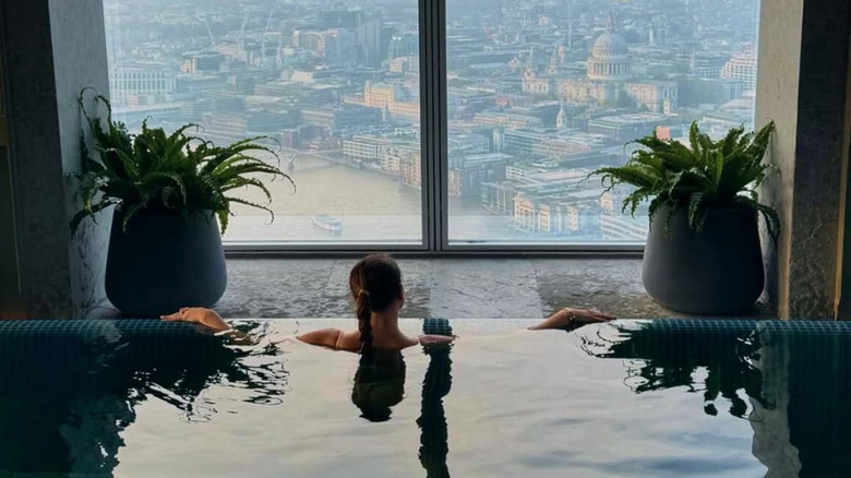 woman looking out window at London skyline from infinity pool