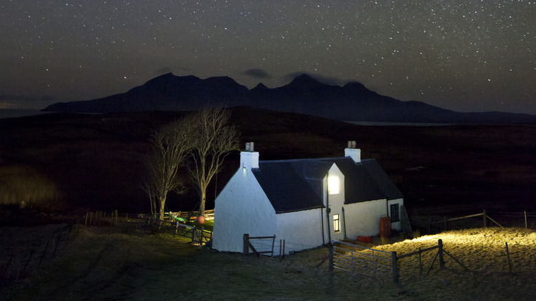 A small house on the Isle of Rum, with light spilling out of its windows, under a night sky full of stars.