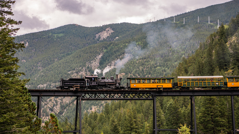 A steam train rides over a bridge through the Rocky Mountains