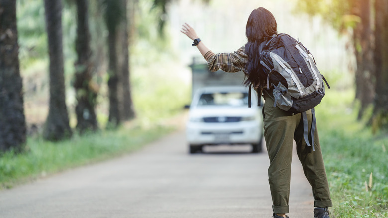 Hitchhiking girl with backpack flagging down car on a road