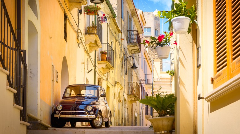 White-washed street with balconies, flower pots, and a parked car in in Termoli.