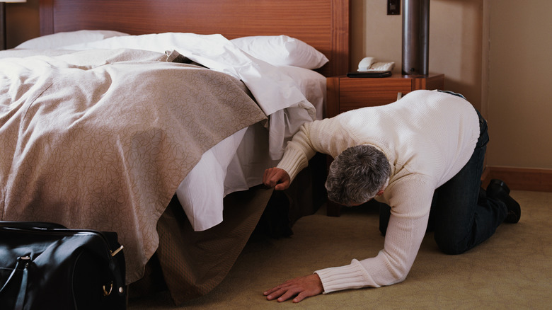 Man searching under hotel bed