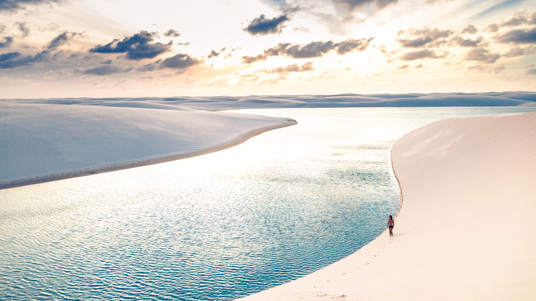 person walks along the dunes near a lagoon at Lençóis Maranhenses National Park