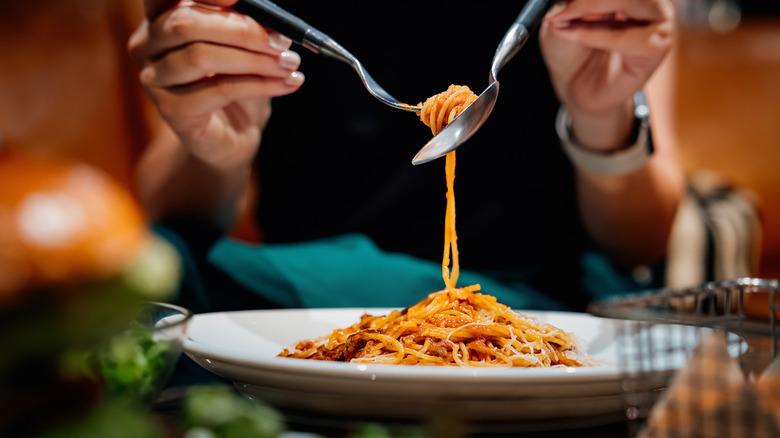 Hands using a spoon and fork to eat pasta