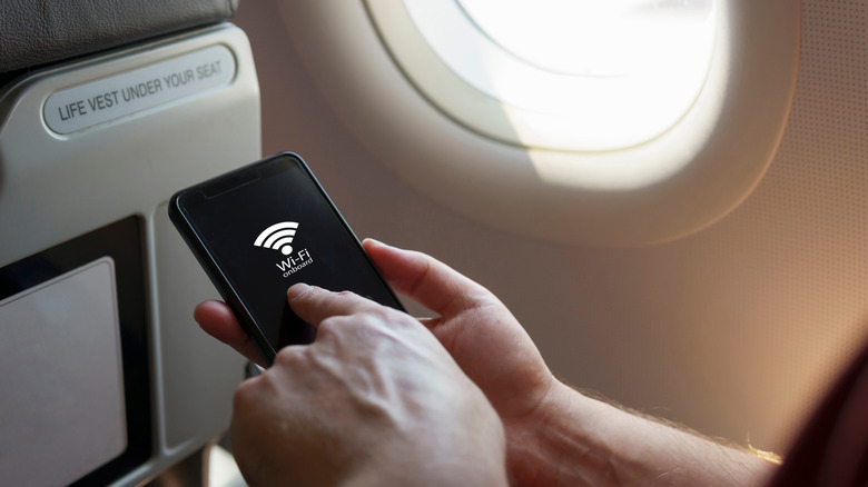 plane passenger's hands holding smartphone showing Wi-Fi icon