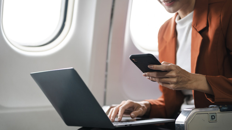 passenger using laptop and phone on airplane