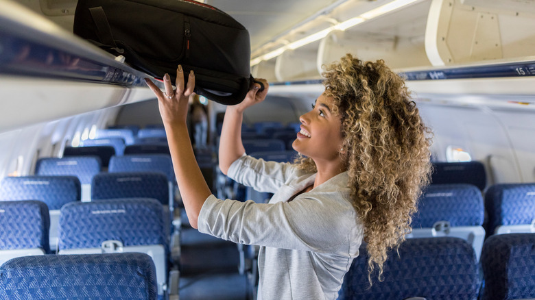 Traveler loading suitcase into overhead bin