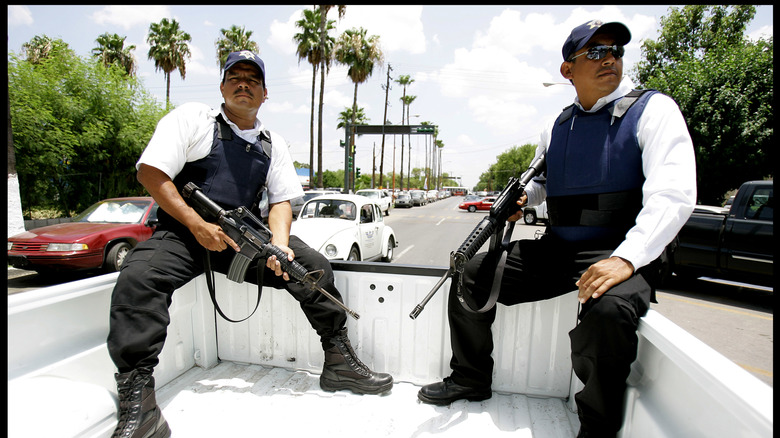 Two Mexican police officers sit in the back of a pickup with assault rifles