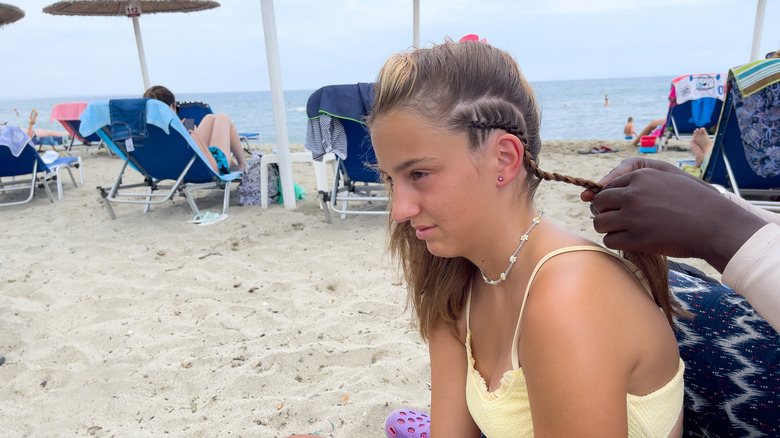 Young girl getting braids on the beach