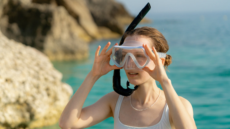 Woman with snorkel gear, blue water, rocks