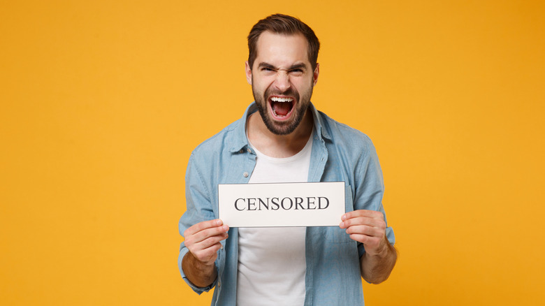 An animated man holds a sign marked censored