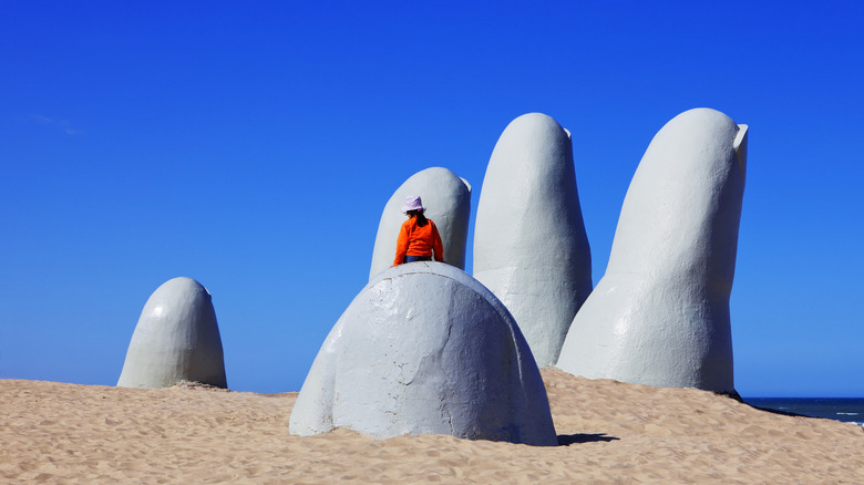 La Mano sculpture rises from the sand in Uruguay person sits on thumb