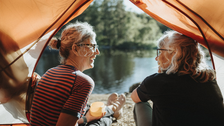 Two older women sit in a tent on the lakeshore