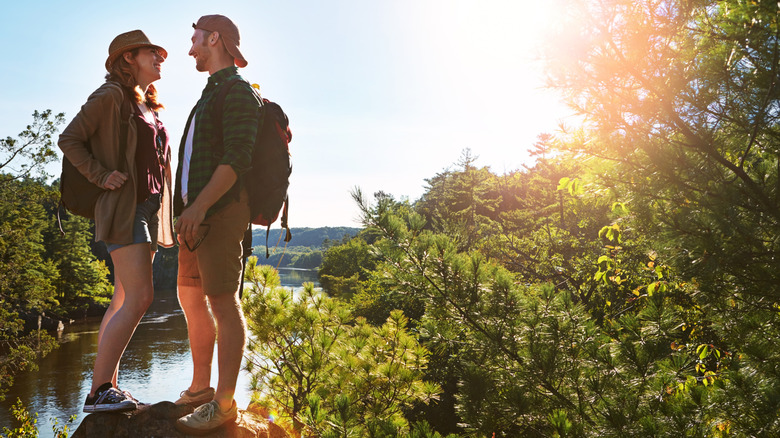 A hiking couple stands on a rock above the forest and lake