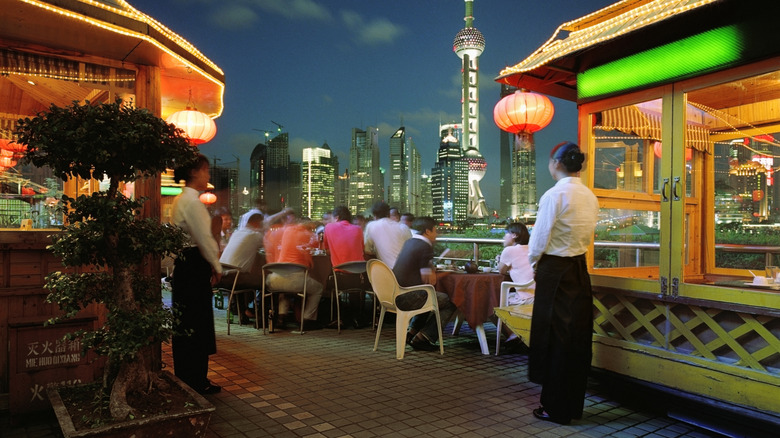 Diners at riverside restaurant in China at night with two servers looking on