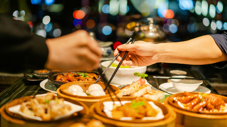 Hands serving food with chopsticks with faded night lights in background