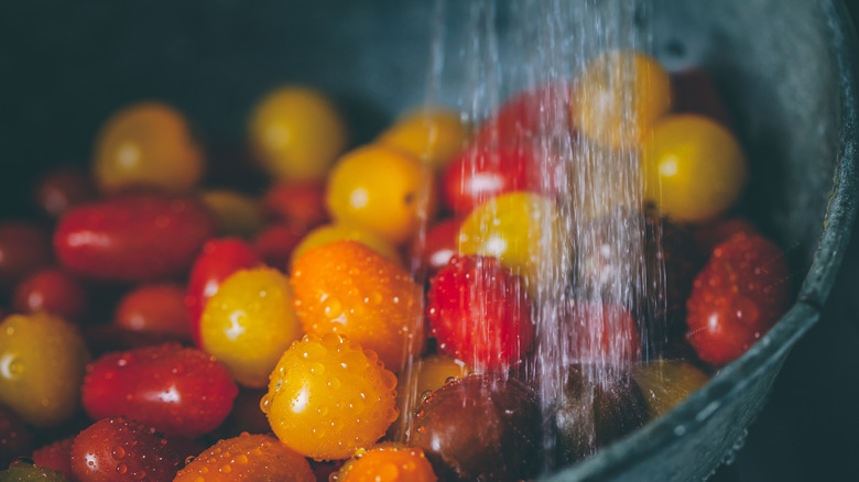 A colorful bowl of tomatoes is getting rinsed off in a sink.