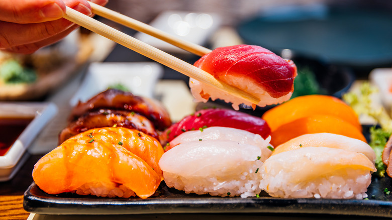 A person grips a chunky piece of sushi with a pair of wooden chopsticks