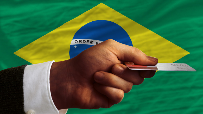 An outstretched hand holds a card in front of a Brazilian flag