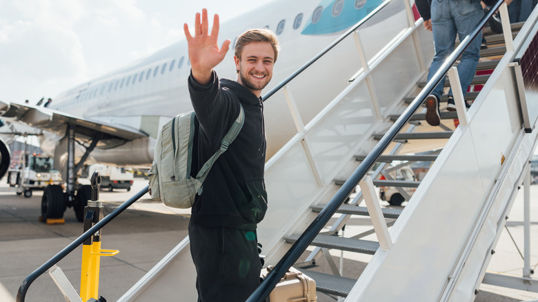 Young traveler waving to camera from plane stairs