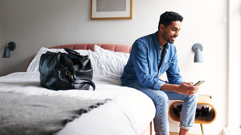 man sitting on bed checking phone in boutique hotel