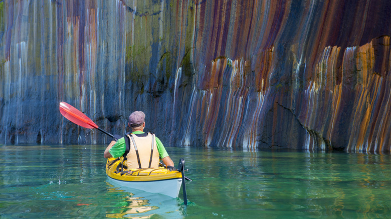 A man kayaks in front of a colorful cliff face on Lake Superior in Michigan's Upper Peninsula