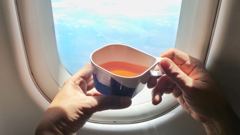 Hands holding tea by airplane window