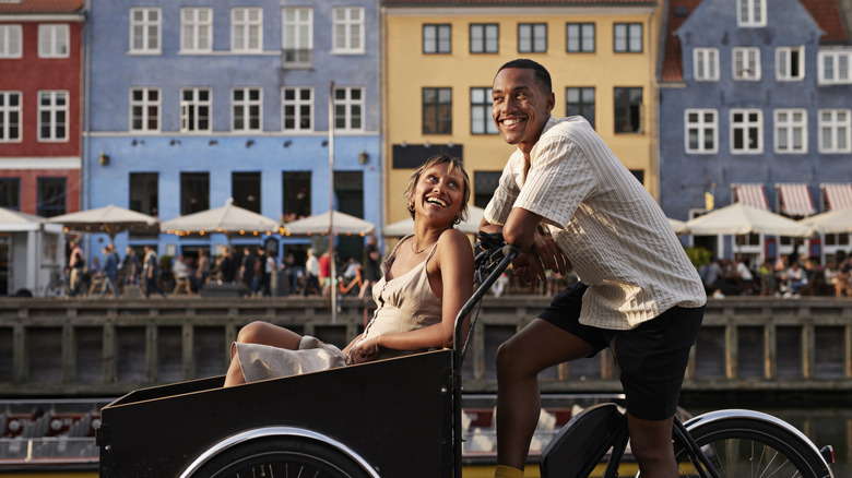 A man and woman smile while riding a cargo bike