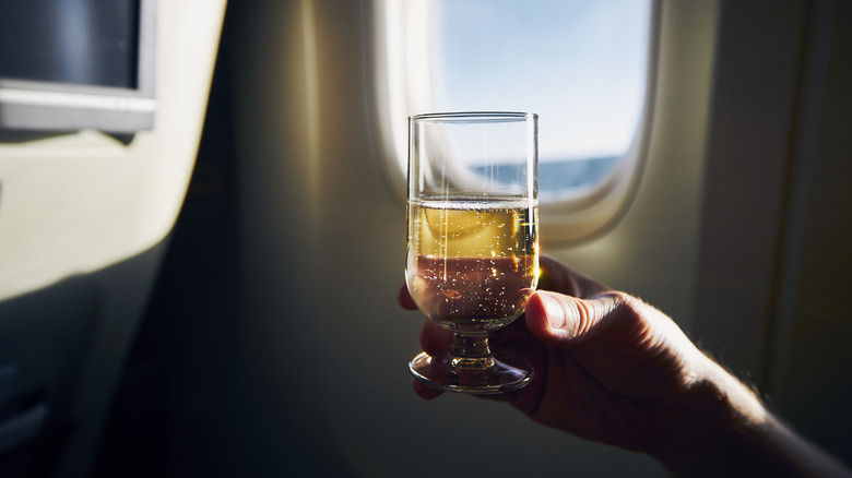 Man holding glass of champagne next to airplane window