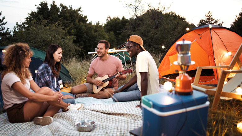 group of friends camping with one playing guitar