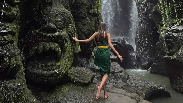 A woman walks toward Taman Beji Griya waterfall.