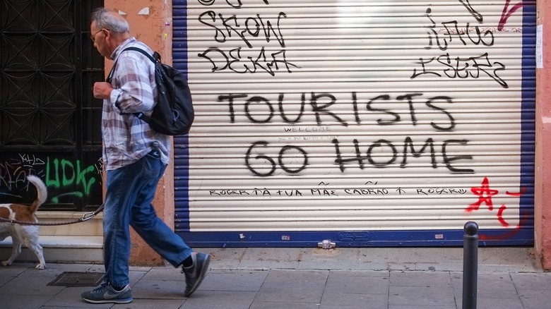 Man walks by "tourists go home" graffiti