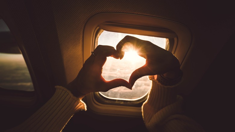 Heart-shaped hands over plane window
