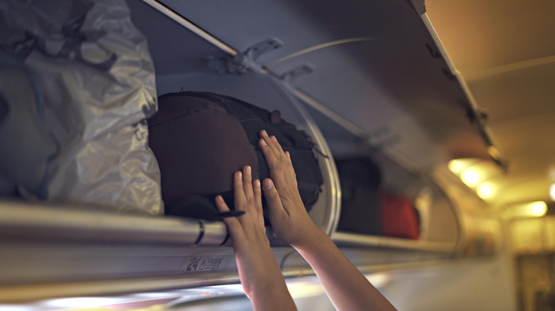 Person storing luggage in overhead bin