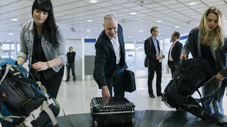 Smiling travelers collect their luggage at airport carousel