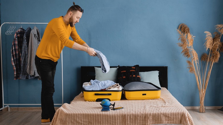 man packing clothes in suitcase