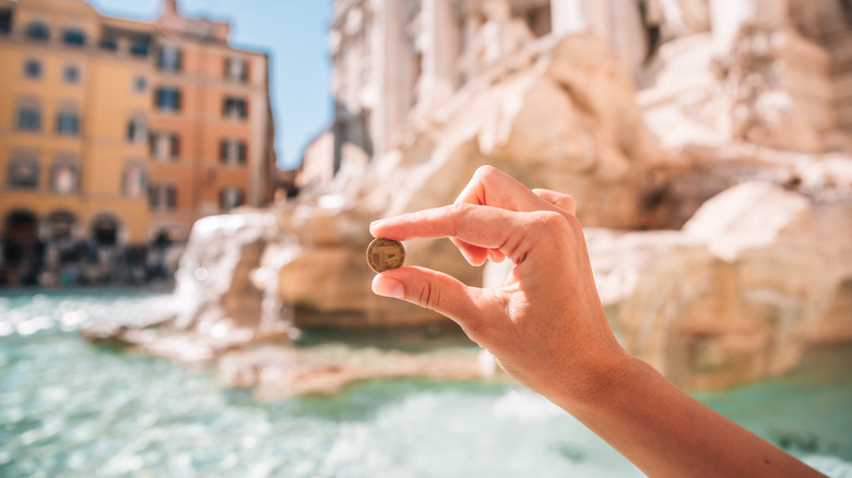 Traveler holding a coin at the Trevi Fountain