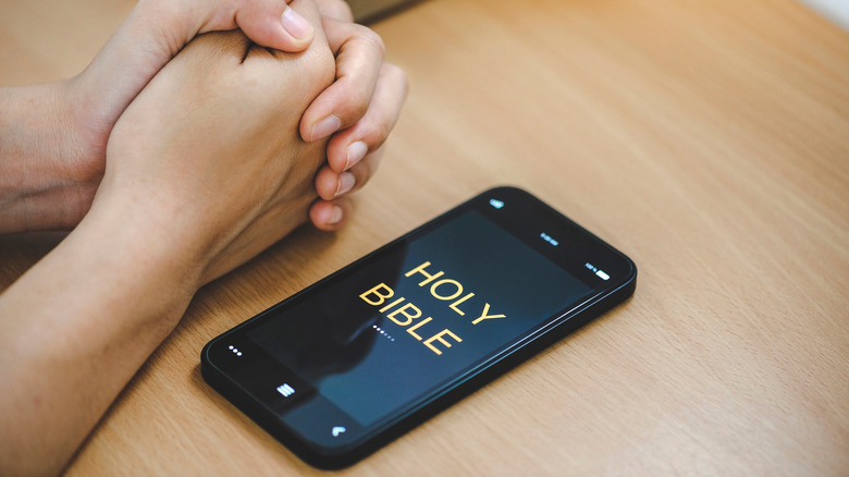 Hands praying Bible on smartphone screen