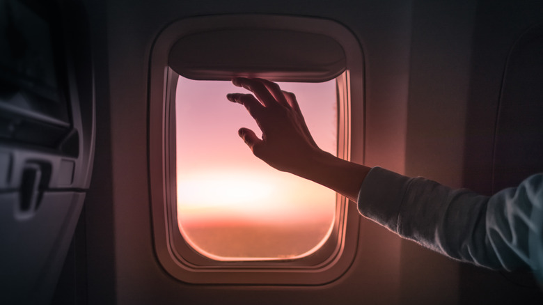 person's hand putting down airplane window