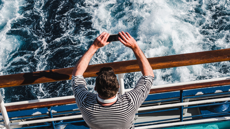 A man photographs frothing water from a cruise ship guardrail